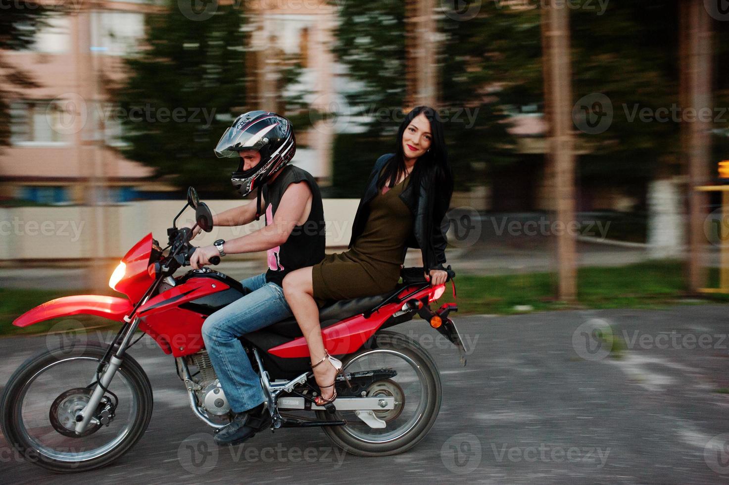 Woman in dress and leather jacket riding a motorbike with another man. photo