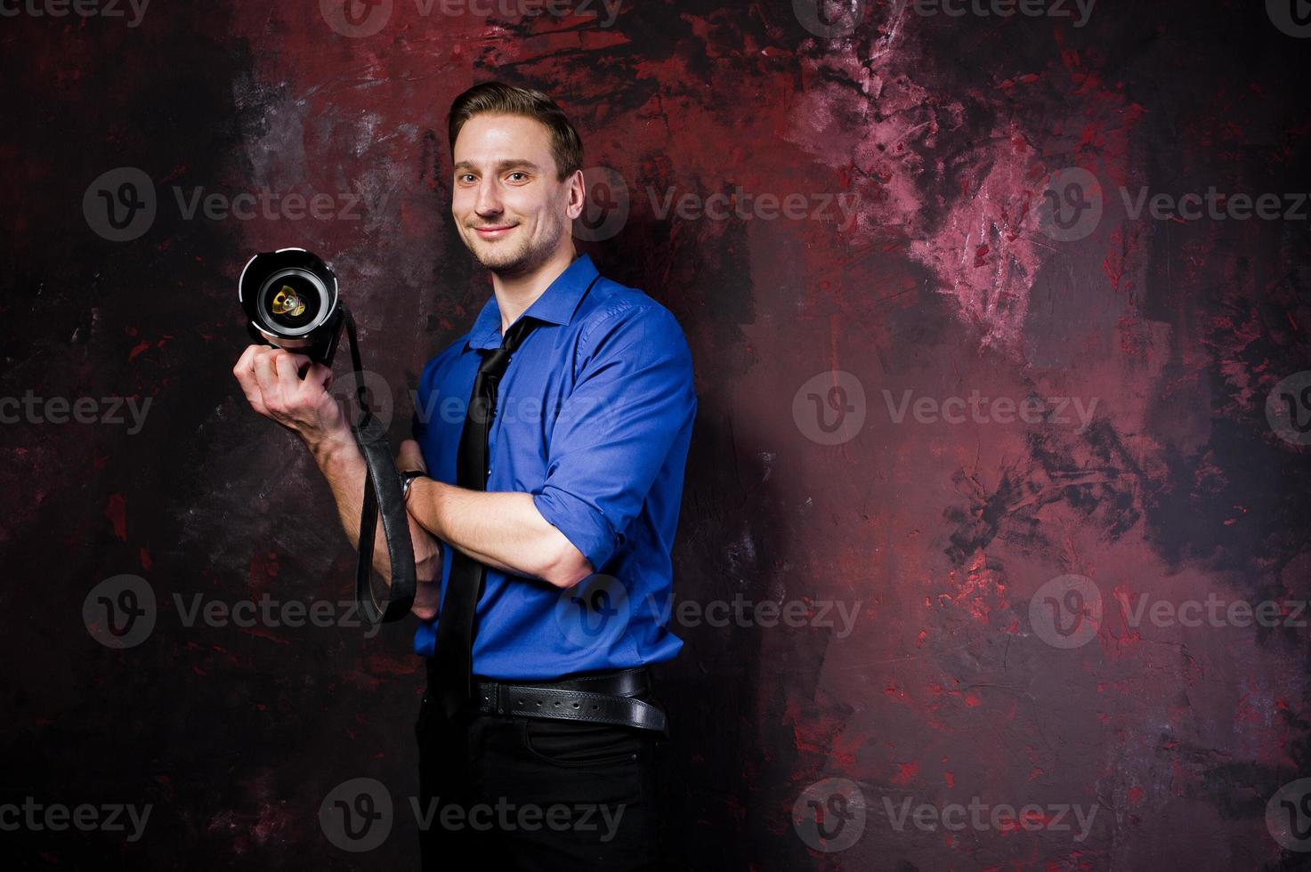 Studio portrait of stylish professional photographer man with camera, wear on blue shirt and necktie. photo