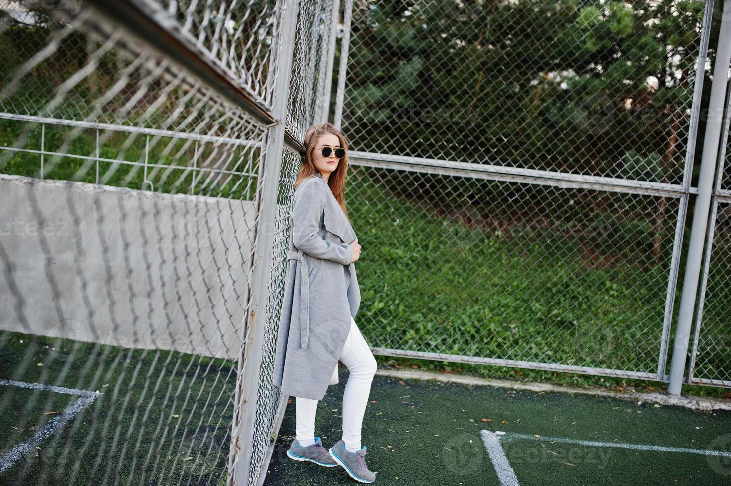 Girl in gray coat with sunglasses at small street stadium. photo