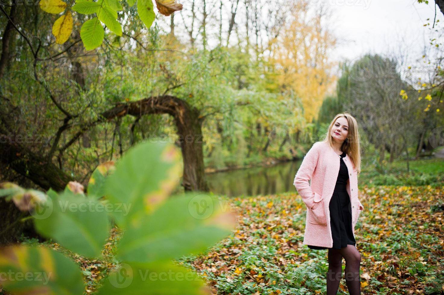 Young blonde girl at pink coat posed on autumn park. photo