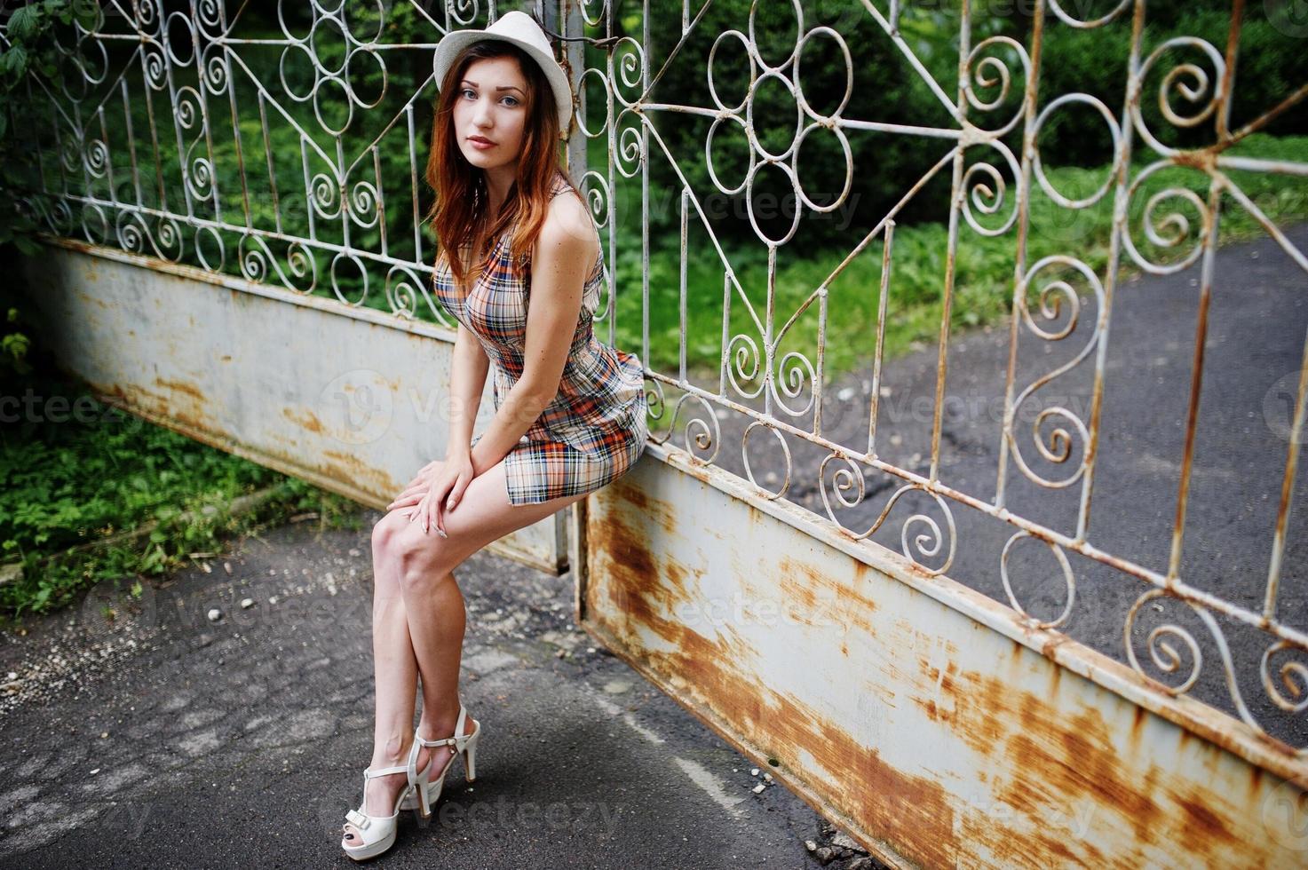 Amazing long legs with hig heels girl wear on hat against iron fence. photo