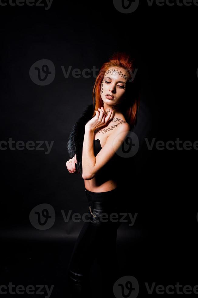 Fashion model red haired girl with originally make up like leopard predator isolated on black. Studio portrait. photo