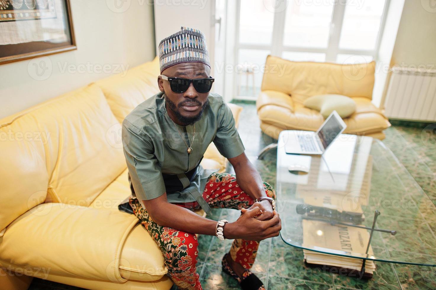 Rich african man sitting on sofa at his appartment. Portrait of successful black man indoor. photo