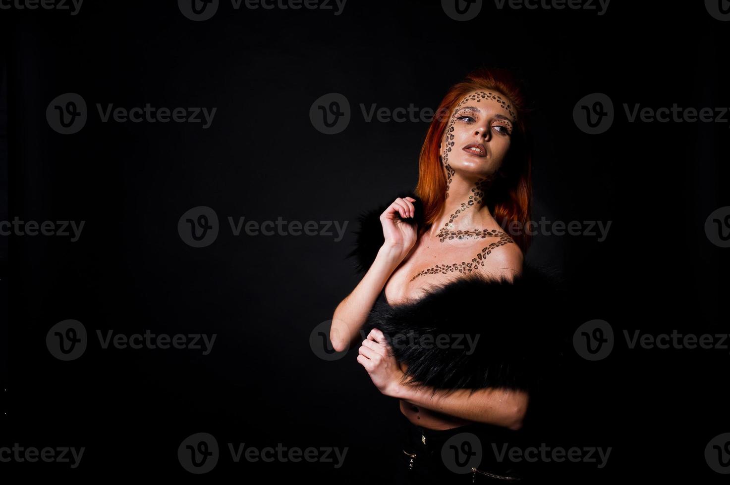 Fashion model red haired girl with originally make up like leopard predator isolated on black. Studio portrait. photo