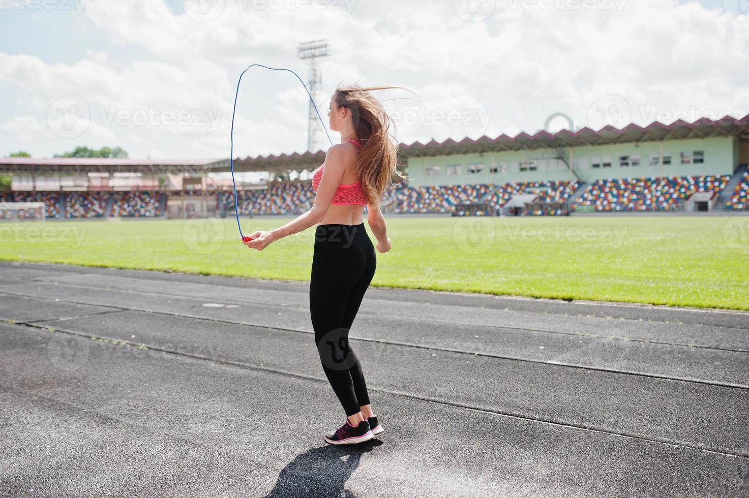 chica deportiva fitness en ropa deportiva en un estadio de fútbol deportes al aire libre. entrenamiento de mujer sexy feliz y saltando con cuerda. foto