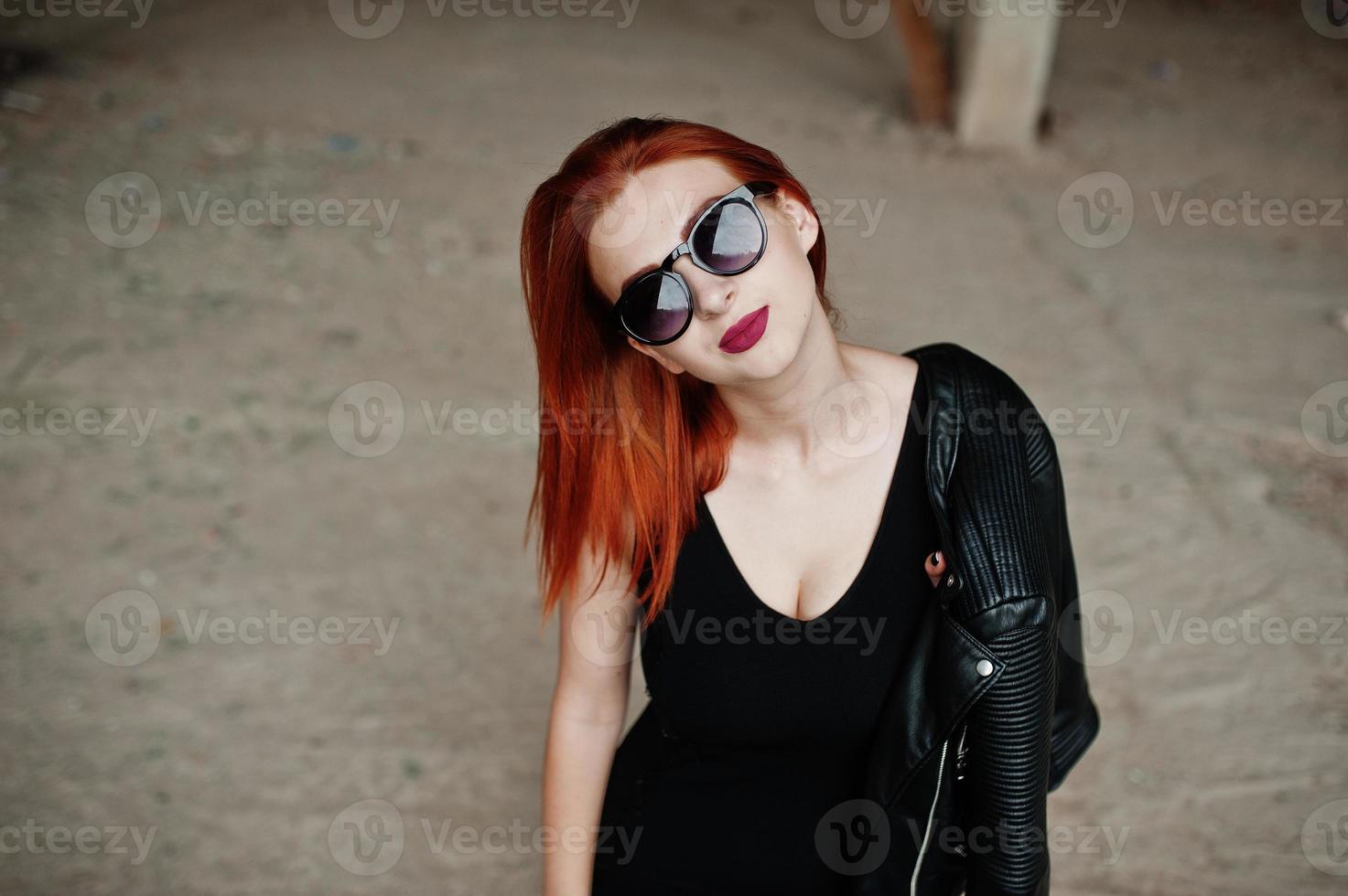 Red haired stylish girl in sunglasses wear in black, against abadoned place. photo