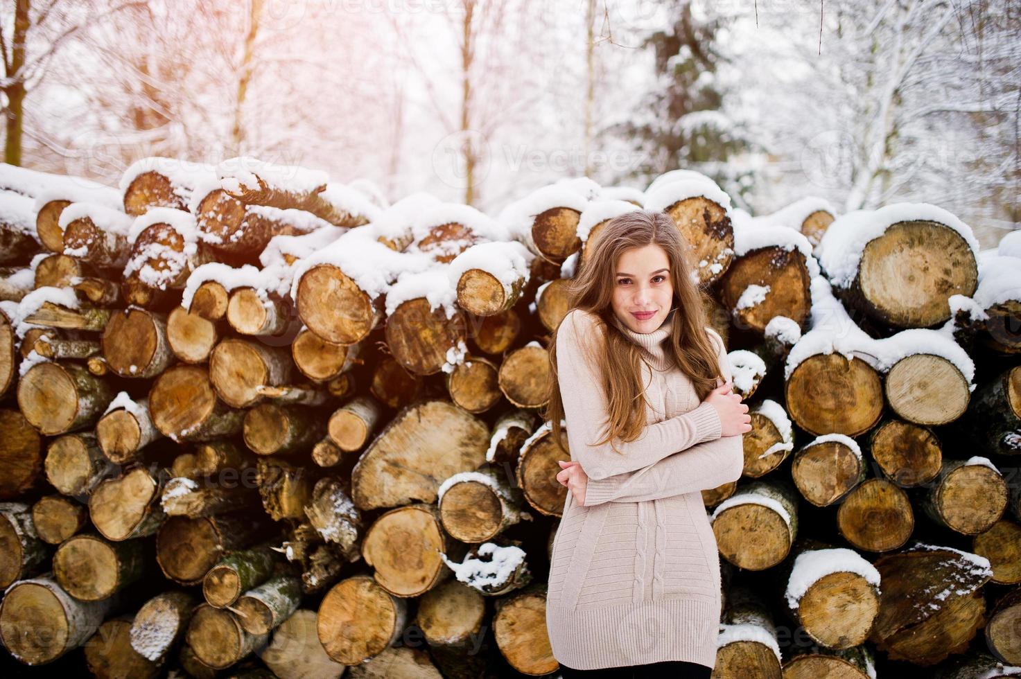 Beautiful brunette girl in winter warm clothing. Model on winter sweater near stump. photo