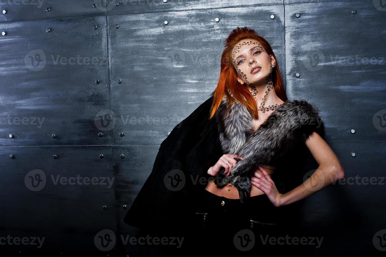 Fashion model red haired girl with originally make up like leopard predator wear on furs against steel wall. Studio portrait. photo