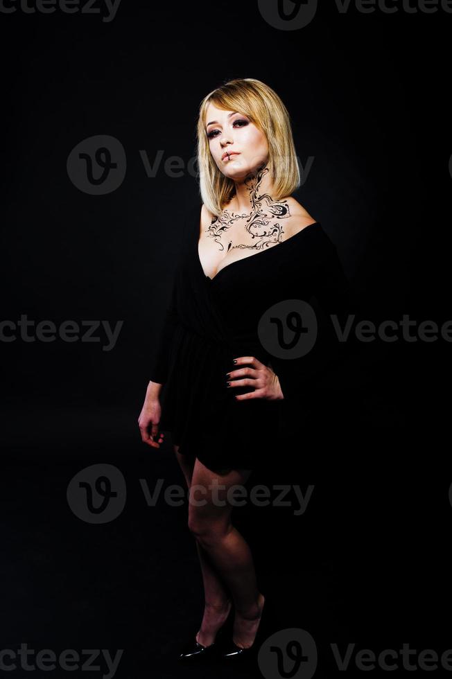 retrato de estudio de una chica rubia con maquillaje original en el cuello, vestida con un vestido negro de fondo oscuro. foto