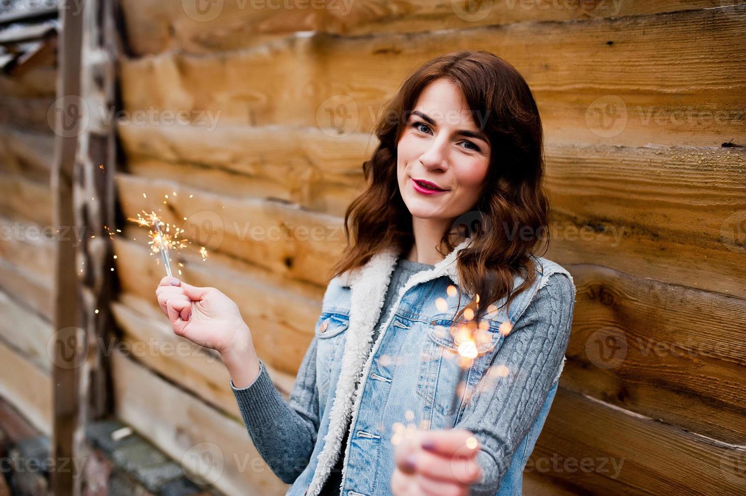 Portrait of brunette girl in jeans jacket with bengal lights in hands. photo