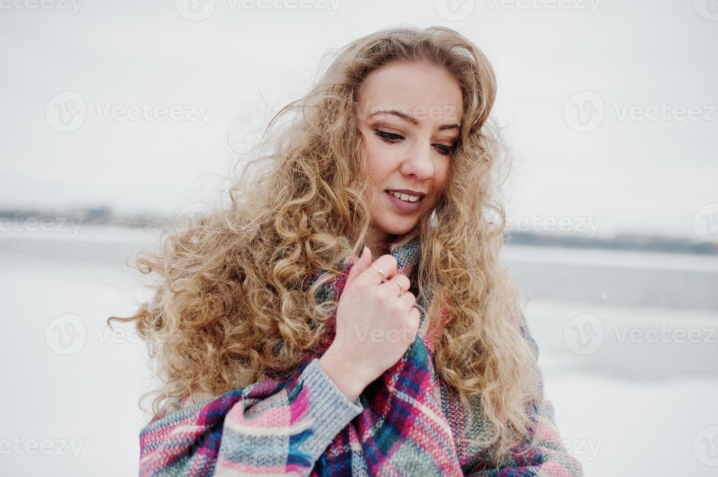 Curly blonde girl in checkered plaid against frozen lake at winter day. photo