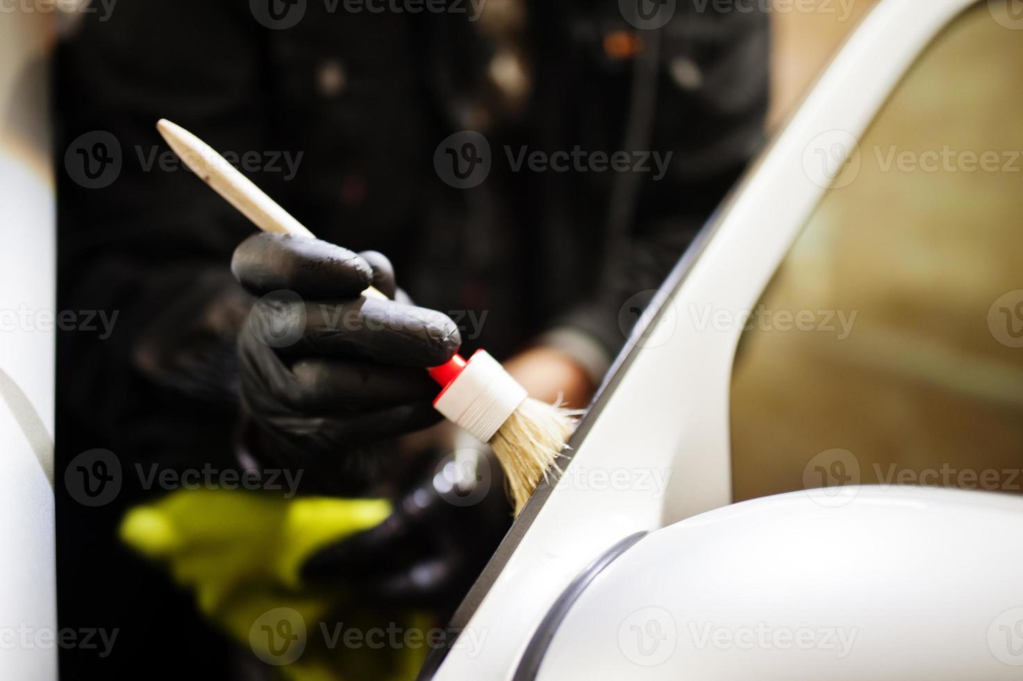 hombre en uniforme y respirador, trabajador del centro de lavado de autos, limpieza del cepillo de limpieza interior del auto. concepto de detalle de coche. foto