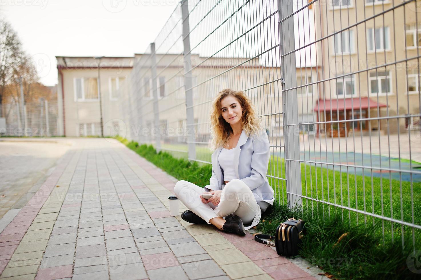 Stylish curly blonde model girl wear on white posing against fence. photo