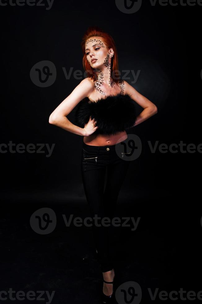 Fashion model red haired girl with originally make up like leopard predator isolated on black. Studio portrait. photo