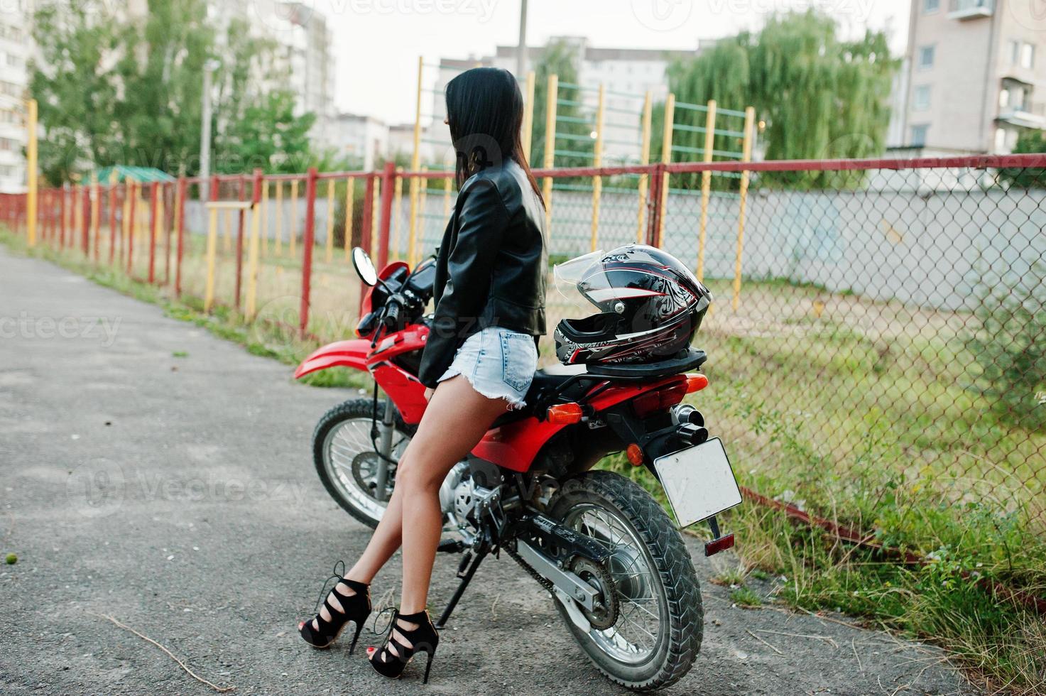 retrato de una mujer genial e impresionante con vestido y chaqueta de cuero negro sentada en una moto roja genial. foto