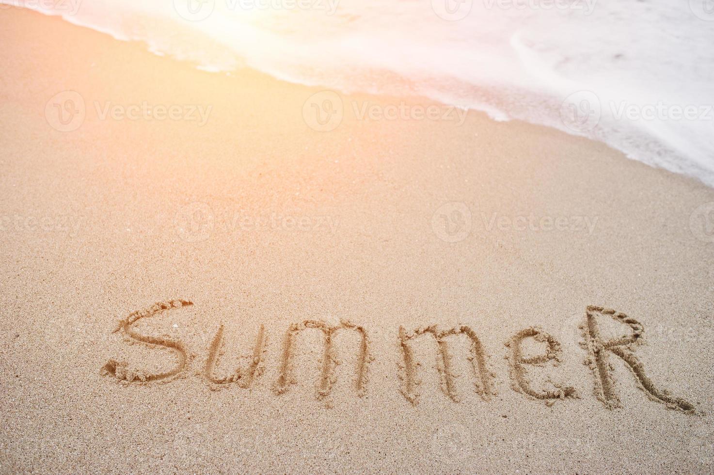 Close-up photo of sand inscription summer by the foamy waves.