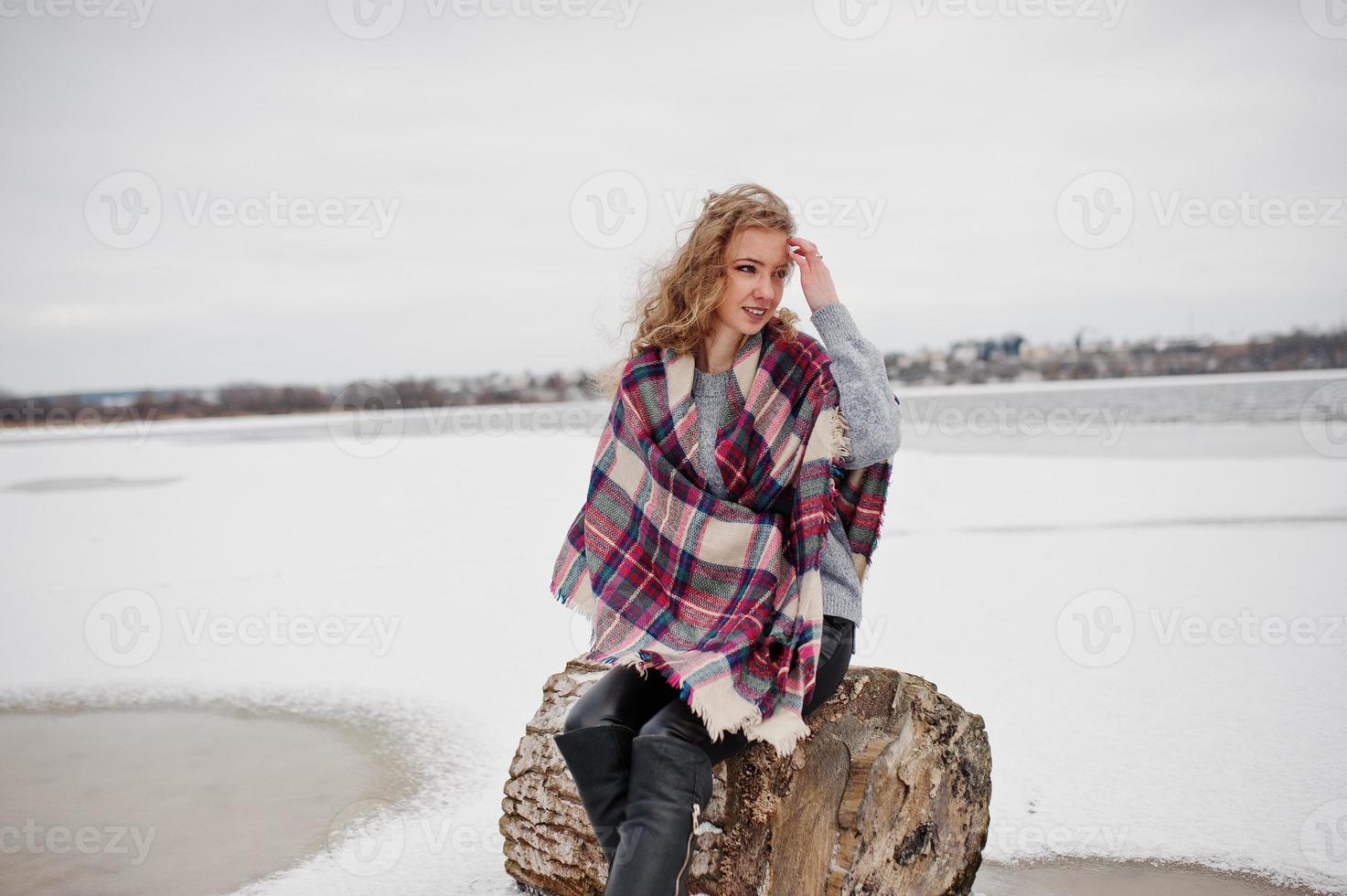 Curly blonde girl in checkered plaid against frozen lake at winter day. photo