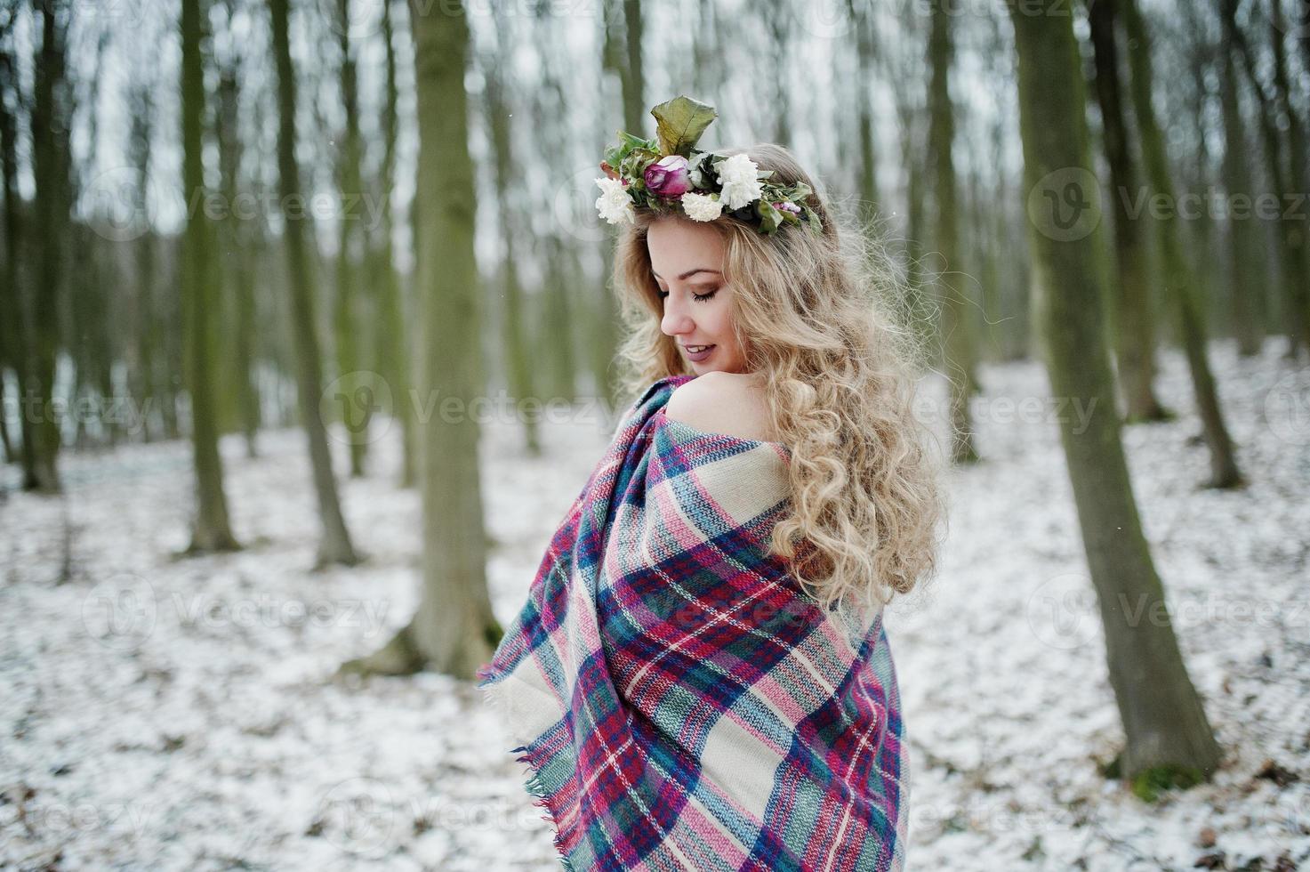 Curly cute blonde girl with wreath in checkered plaid at snowy forest in winter day. photo