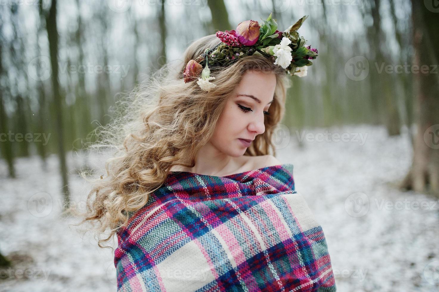 Curly cute blonde girl with wreath in checkered plaid at snowy forest in winter day. photo