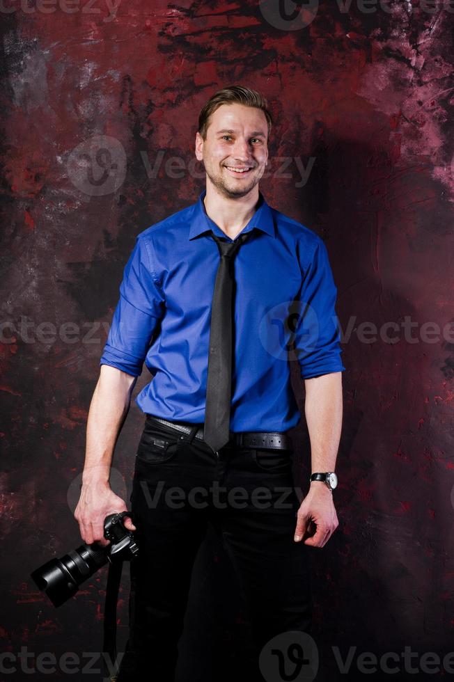 Studio portrait of stylish professional photographer man with camera, wear on blue shirt and necktie. photo