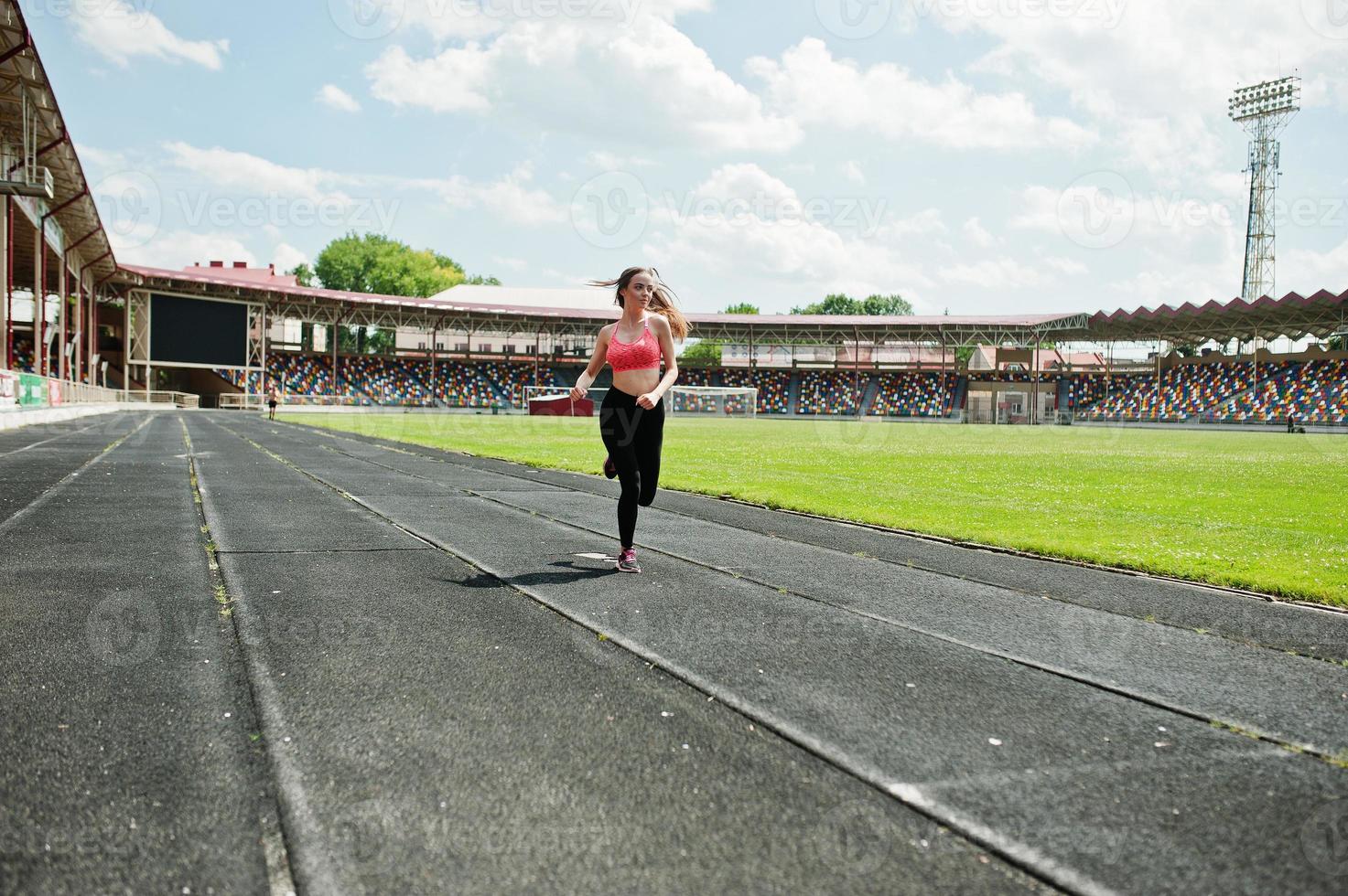 Fitness sporty girl in sportswear at stadium outdoor sports. Happy sexy woman running on athletic track treadmill on stadium. photo