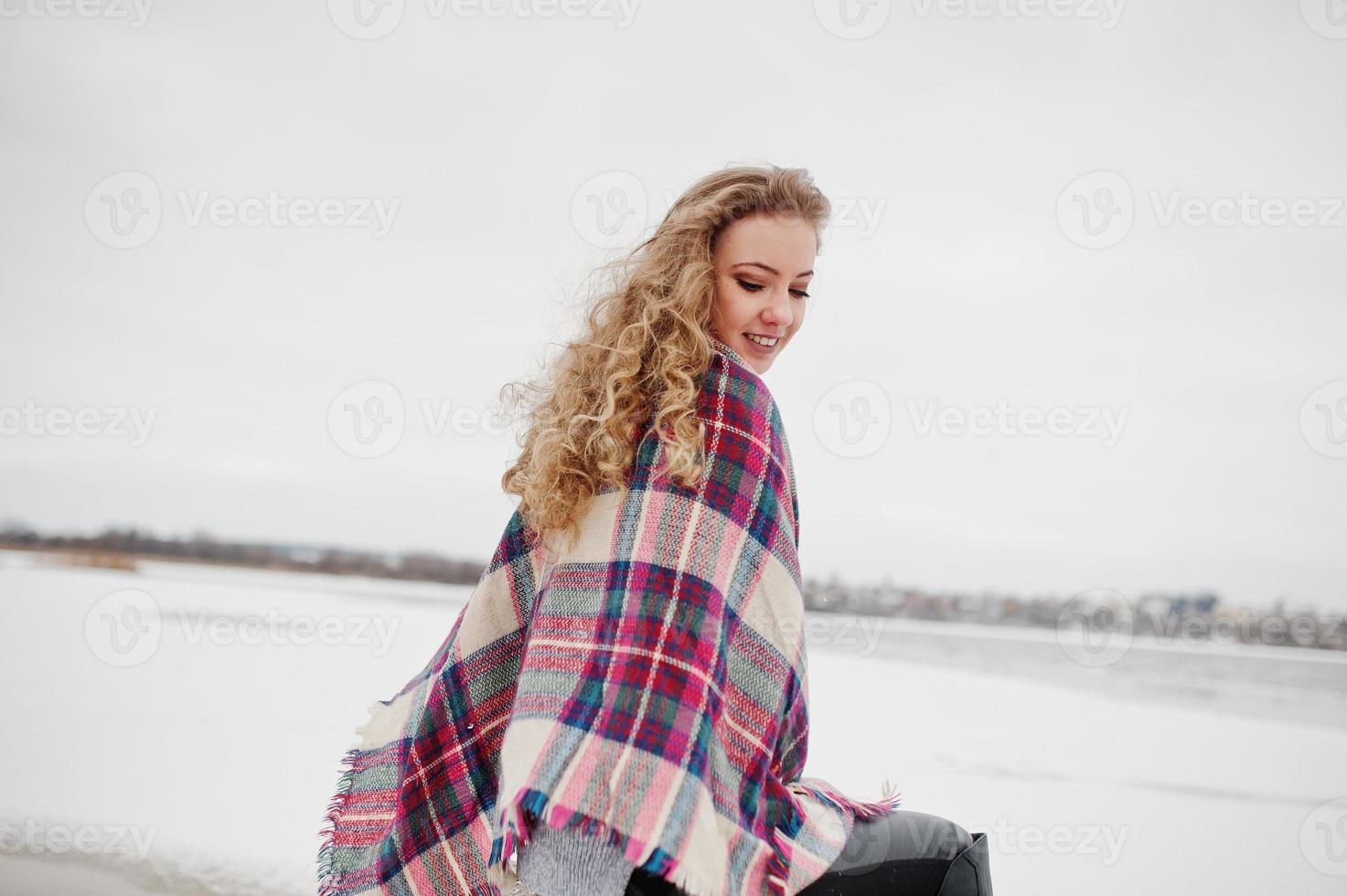 Curly blonde girl in checkered plaid against frozen lake at winter day. photo