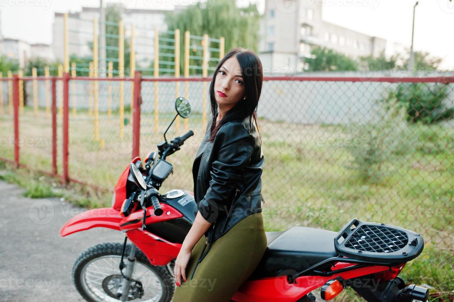 Portrait of a cool and awesome woman in dress and black leather jacket sitting on a cool red motorbike. photo