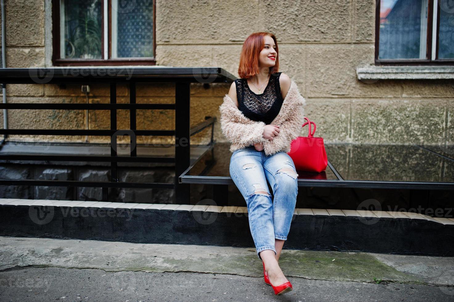 chica pelirroja con bolso rojo posó en la calle de la ciudad. foto