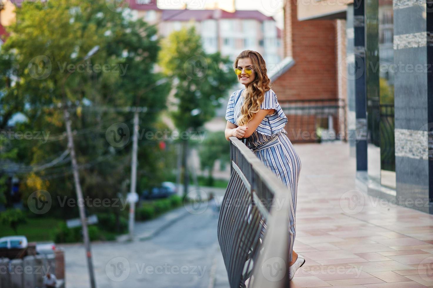 retrato de una mujer joven perfecta con poses de rayas en general y gafas de sol amarillas en un balcón de un edificio moderno en una ciudad. foto