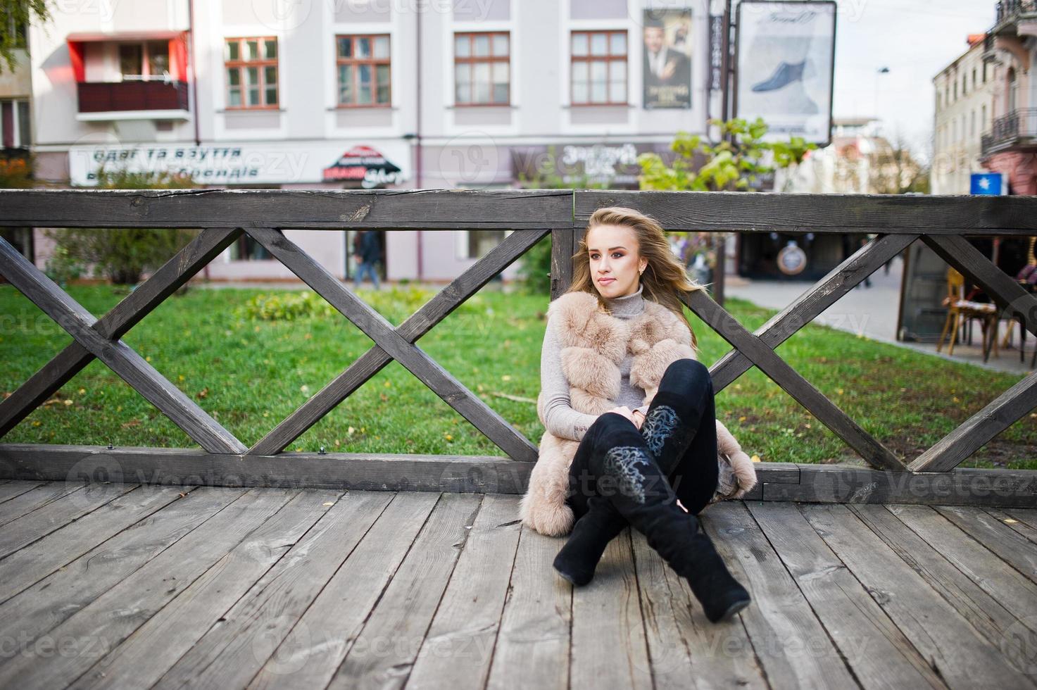 chica rubia en abrigo de piel sentado en el piso de madera al aire libre. foto
