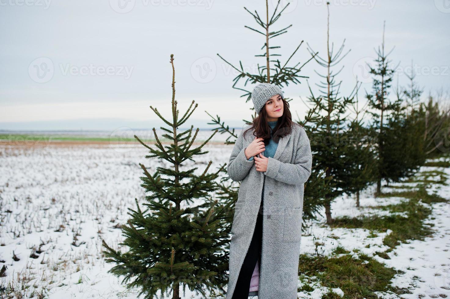 Portrait of gentle girl in gray coat and hat against new year tree outdoor. photo