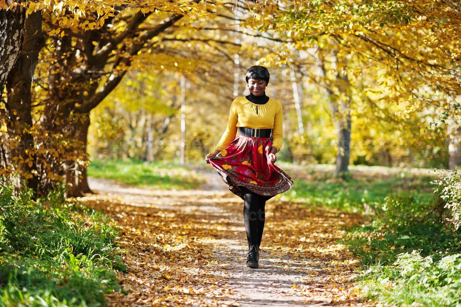 niña afroamericana con vestido amarillo y rojo en el parque de otoño dorado. foto