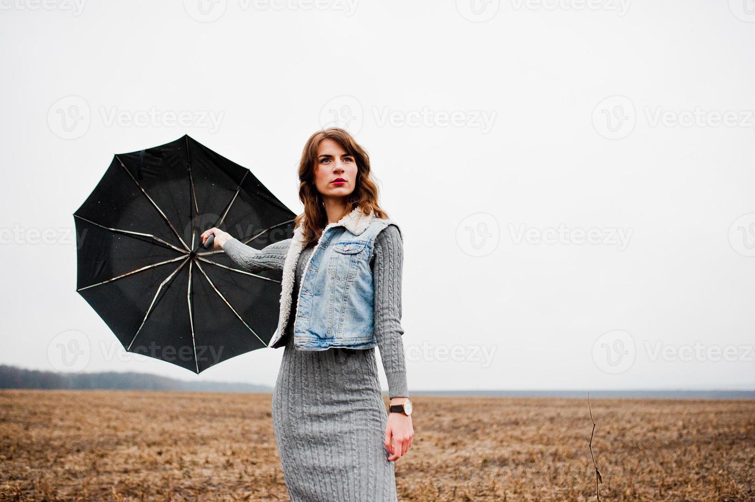 Portrait of brunette curly girl in jeans jacket with black umbrella at field. photo