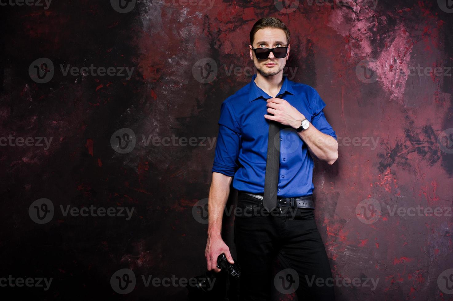 Studio portrait of stylish professional photographer man with camera, wear on blue shirt and necktie, sunglasses. photo