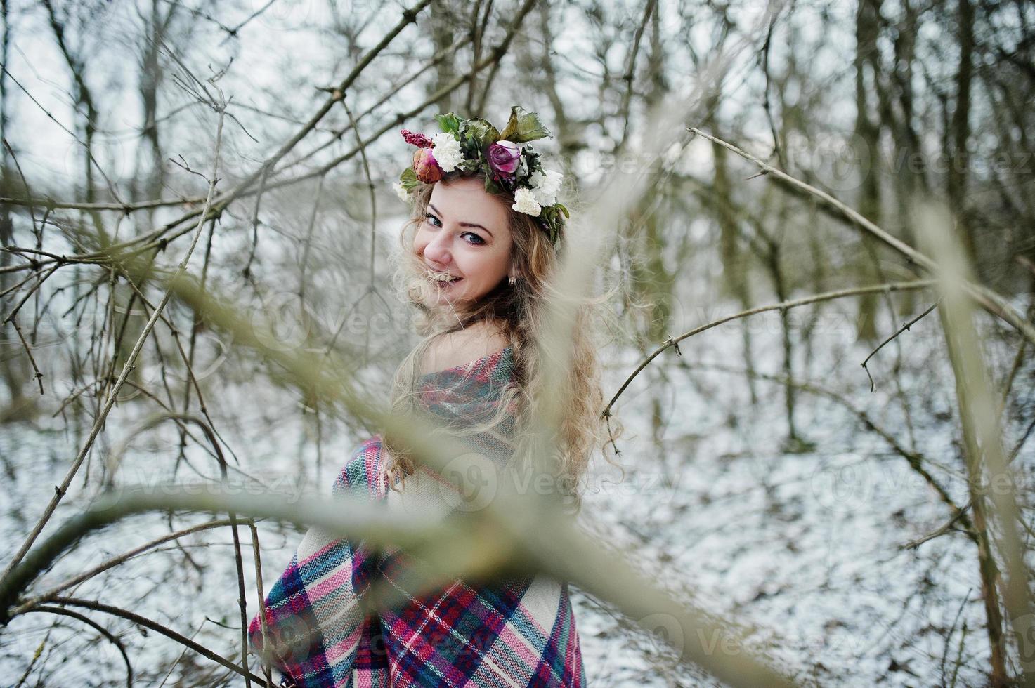 Curly cute blonde girl with wreath in checkered plaid at snowy forest in winter day. photo