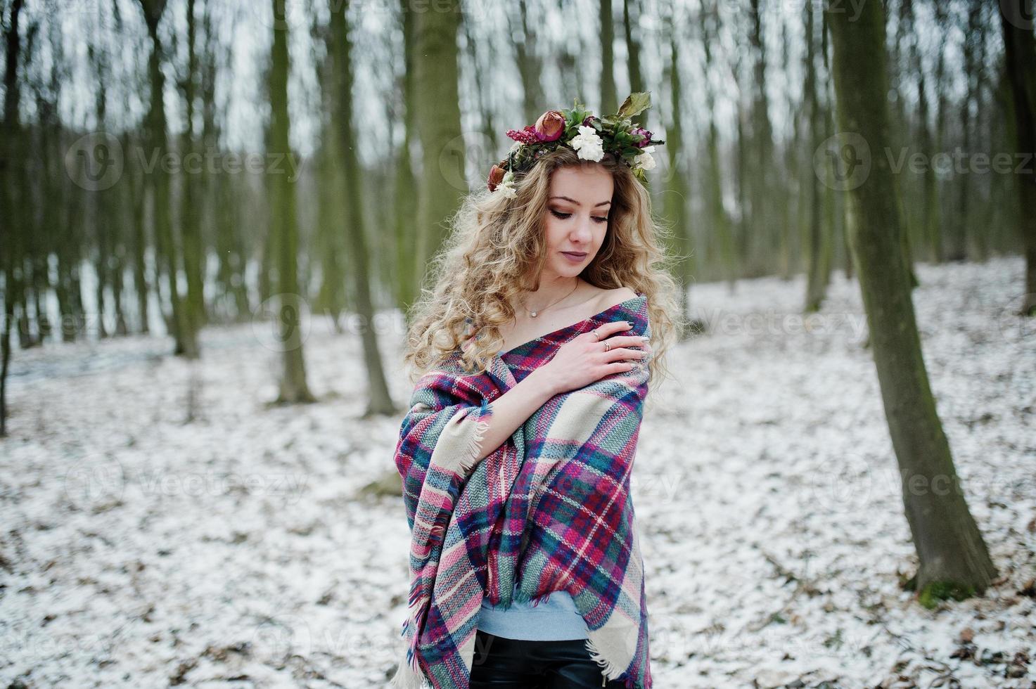Curly cute blonde girl with wreath in checkered plaid at snowy forest in winter day. photo