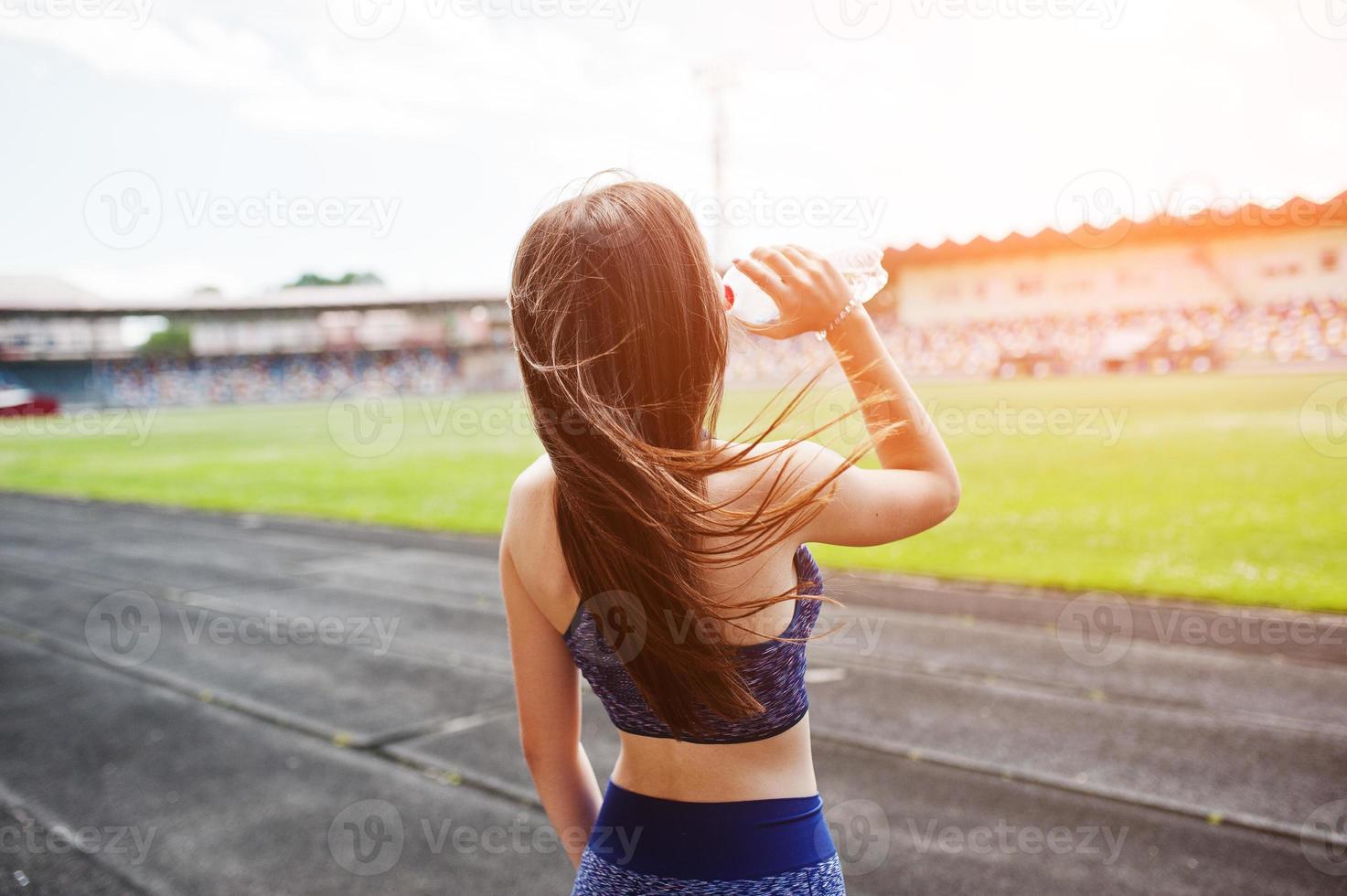Portrait of a fit woman drinking water after running in the stadium. photo