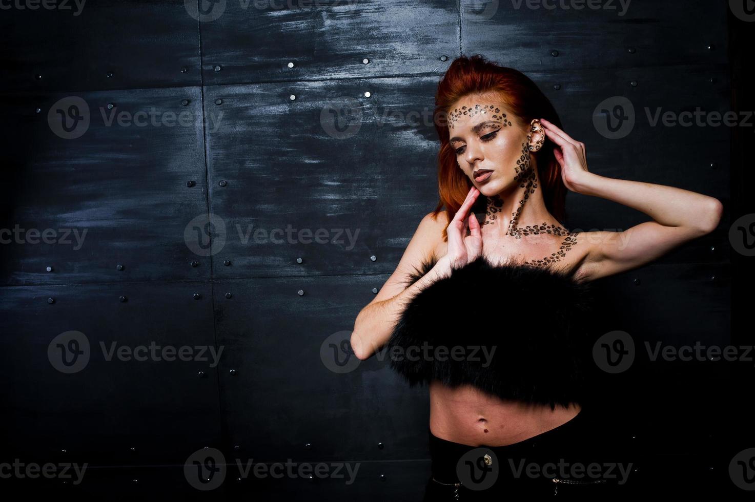 Fashion model red haired girl with originally make up like leopard predator against steel wall. Studio portrait. photo
