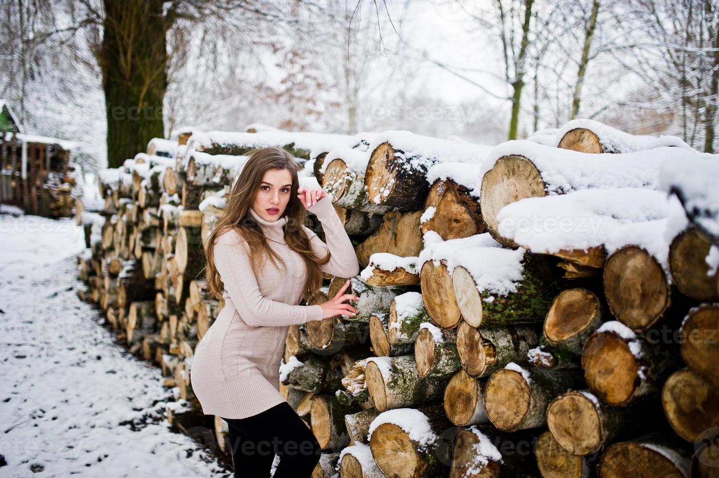 Beautiful brunette girl in winter warm clothing. Model on winter sweater near stump. photo