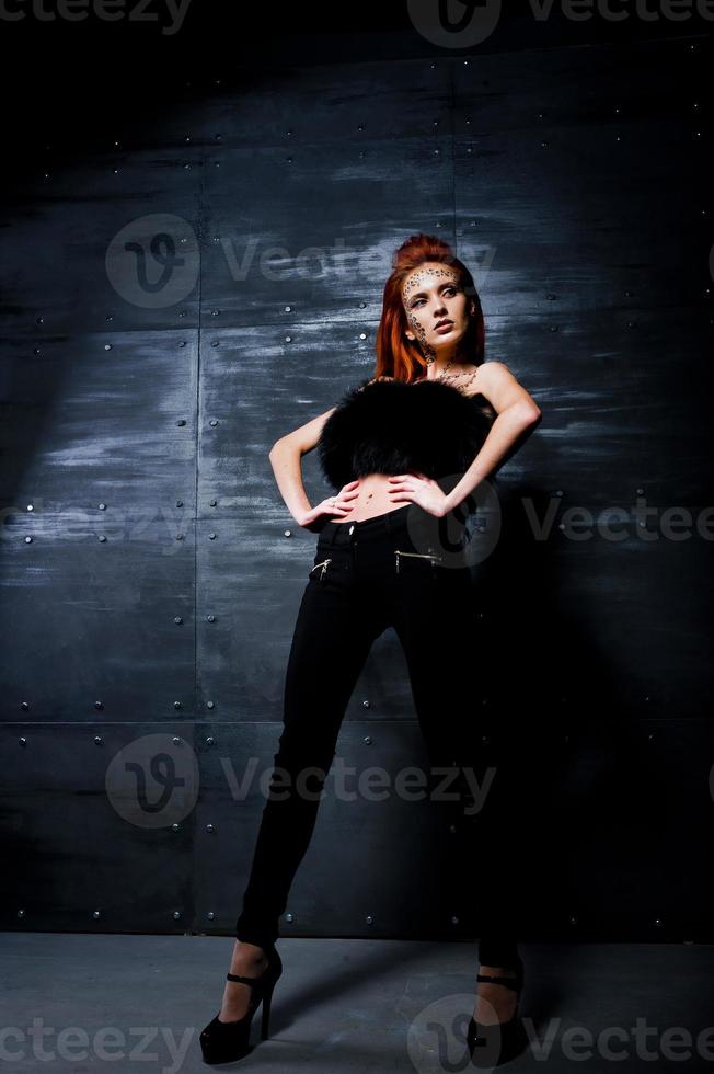 Fashion model red haired girl with originally make up like leopard predator against steel wall. Studio portrait. photo