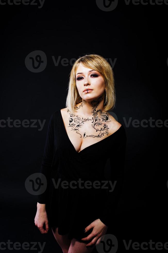 Studio portrait of blonde girl with originally make up on neck, wear on black dress at dark background. photo