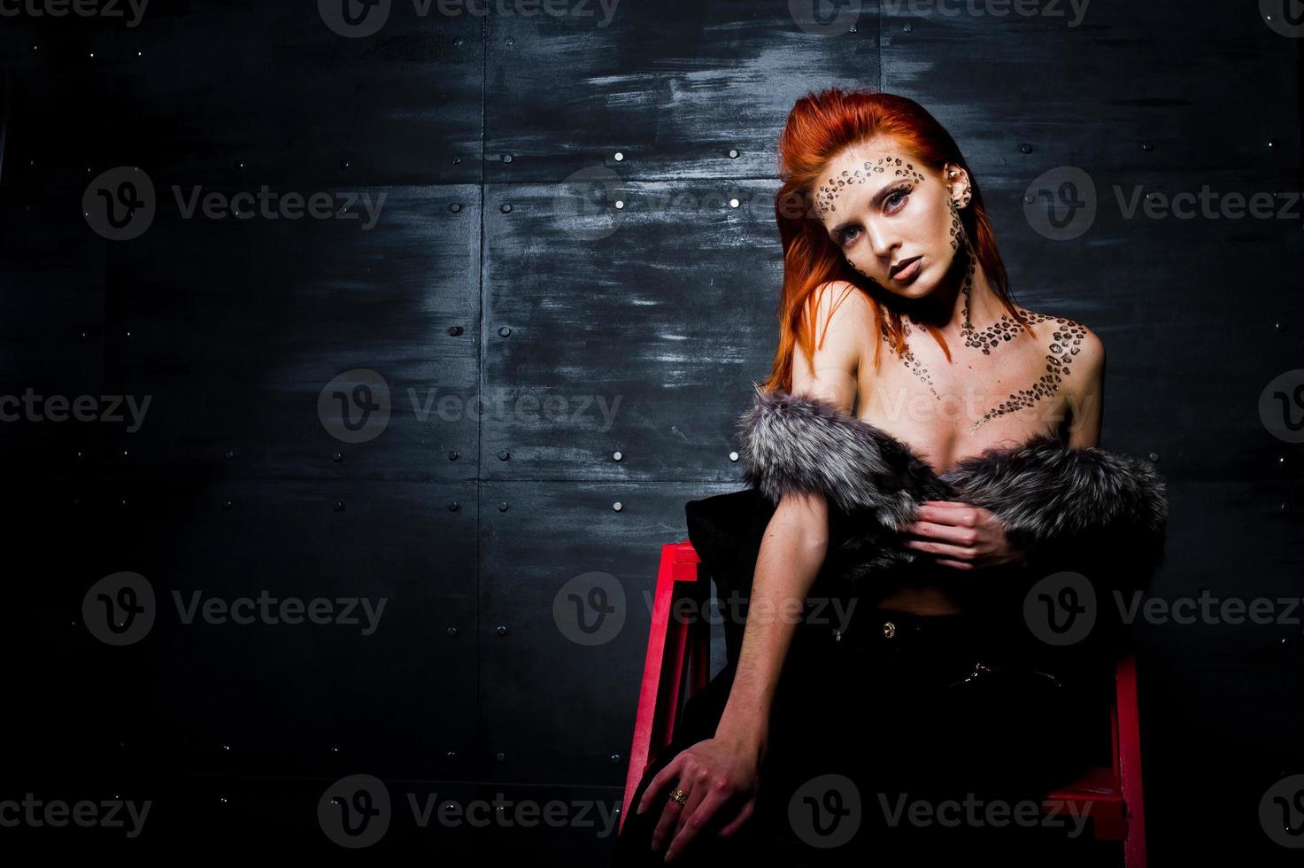 Fashion model red haired girl with originally make up like leopard predator against steel wall. Studio portrait on ladder. photo