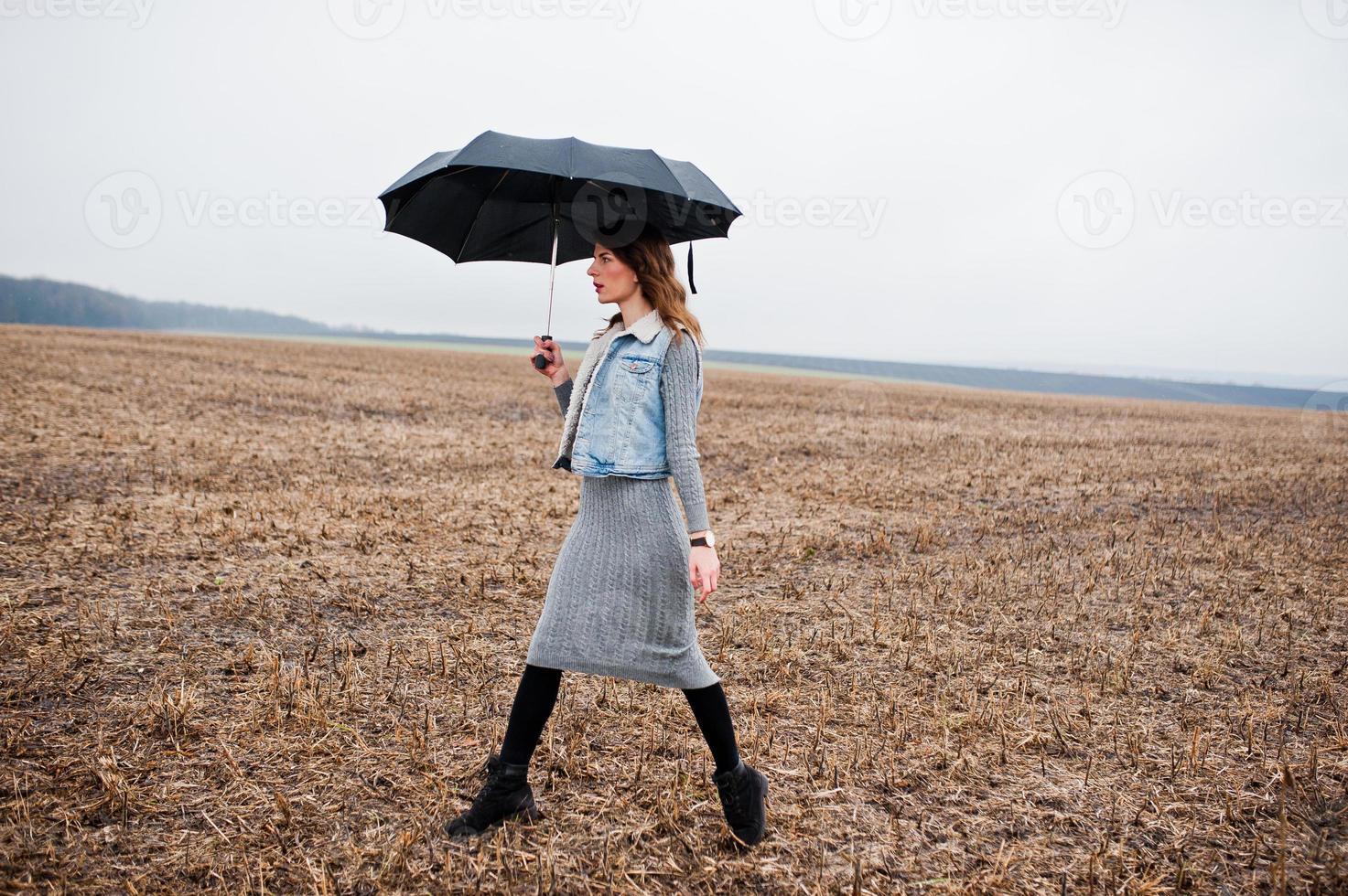 Portrait of brunette curly girl in jeans jacket with black umbrella at field. photo