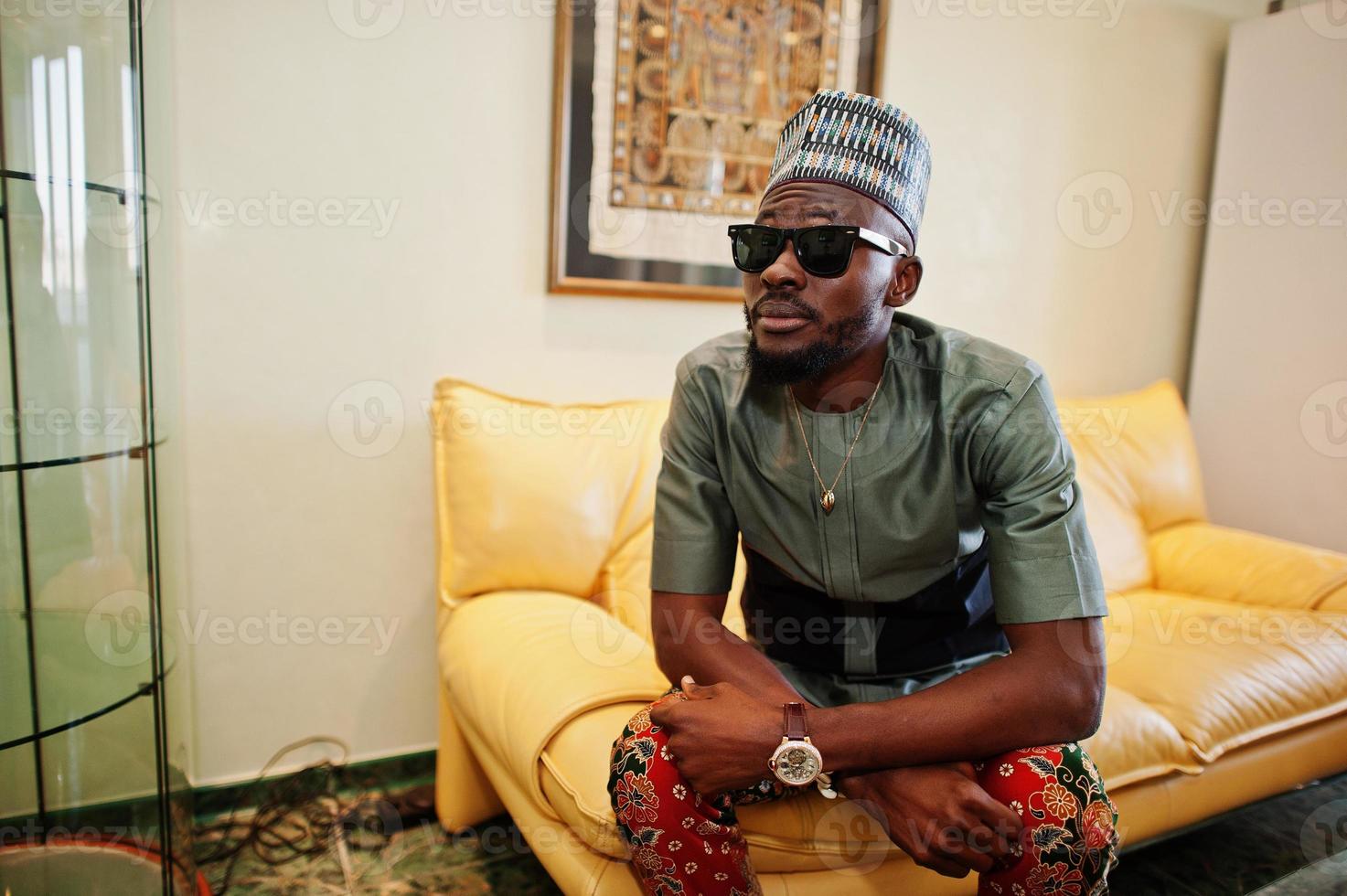Rich african man sitting on sofa at his appartment. Portrait of successful black man indoor. photo