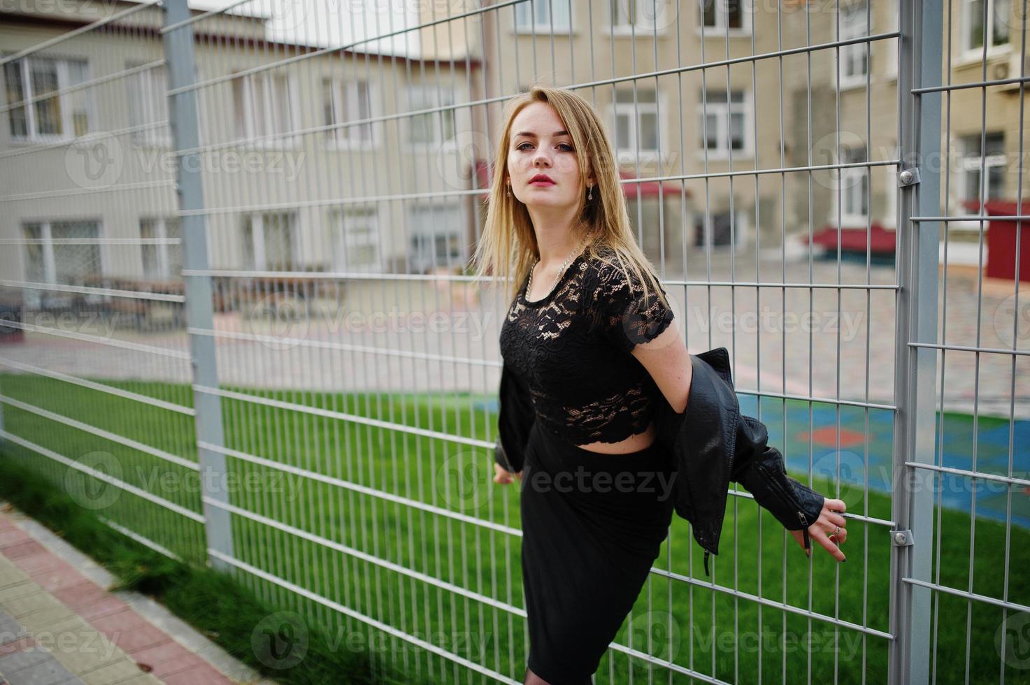 Elegant blonde girl wear on black posing at streets of town against iron cage. photo