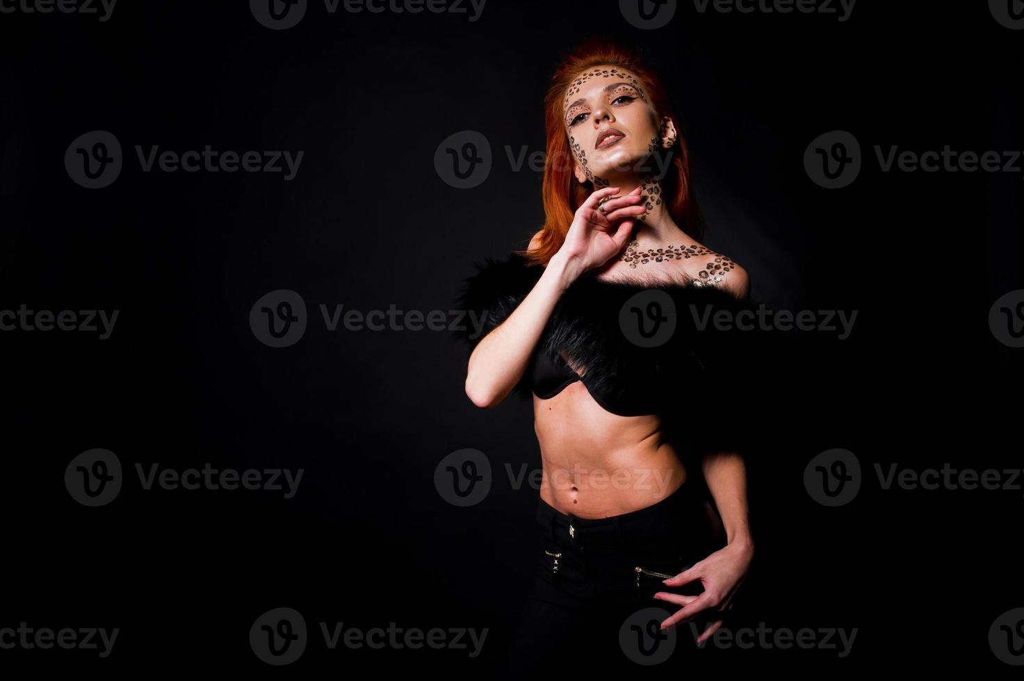 Fashion model red haired girl with originally make up like leopard predator isolated on black. Studio portrait. photo