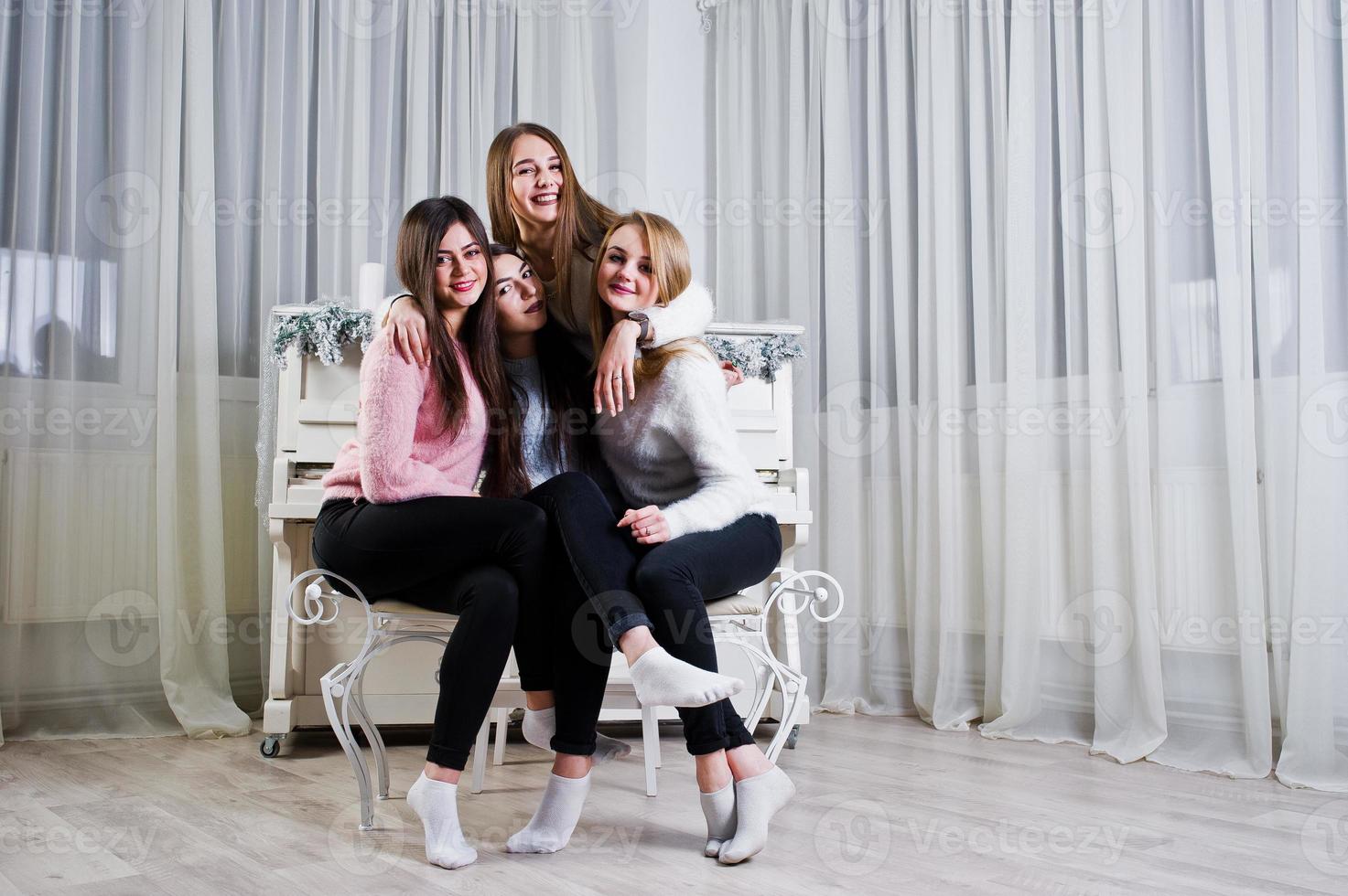 Four cute friends girls wear on warm sweaters and black pants against old piano with christmas decoration at white room. photo