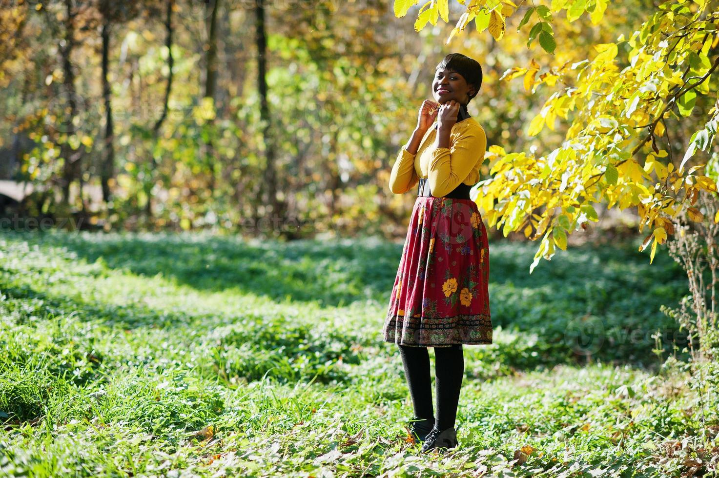 niña afroamericana en vestido amarillo y rojo en el parque de otoño. foto