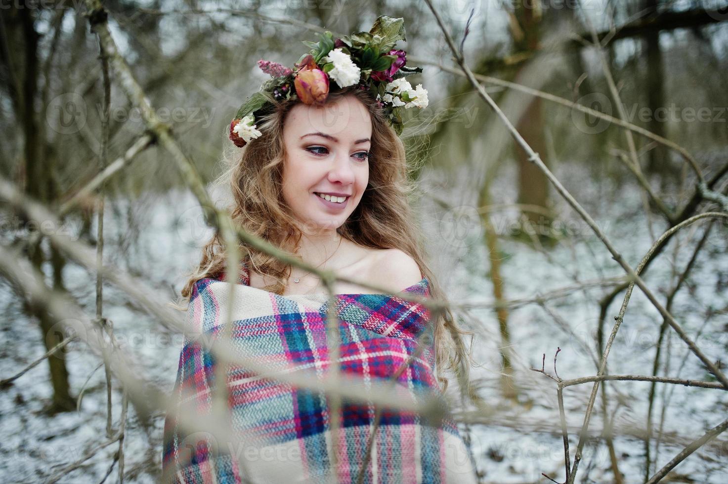 Curly cute blonde girl with wreath in checkered plaid at snowy forest in winter day. photo