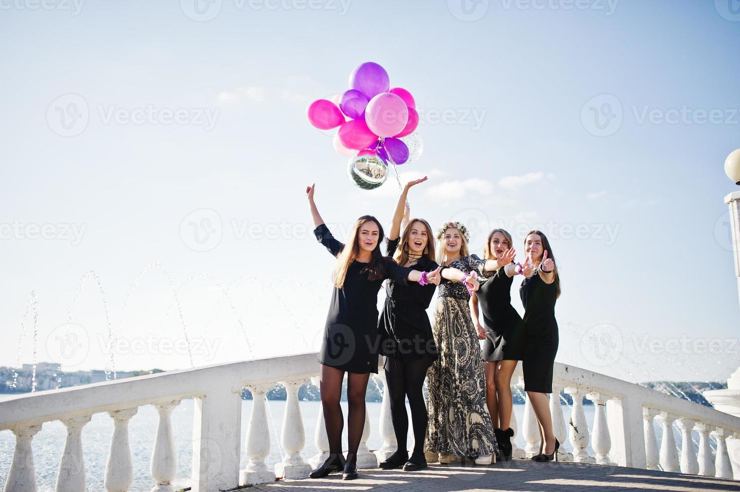 Five girls wear on black walking with balloons at hen party against lake. photo